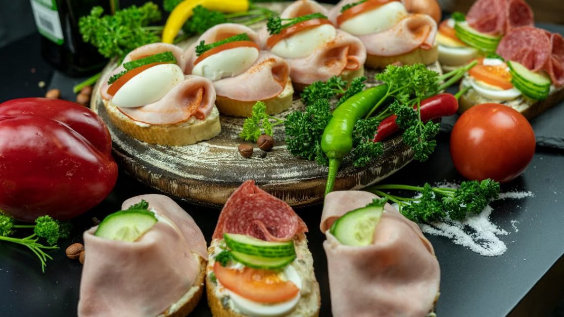 Delicious open-faced sandwiches with ham, eggs, and veggies on a wooden platter.