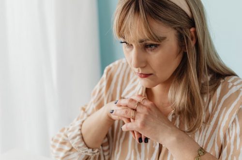 Pensive woman indoors, hands clasped, looking contemplative. Captured in natural light.