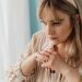 Pensive woman indoors, hands clasped, looking contemplative. Captured in natural light.